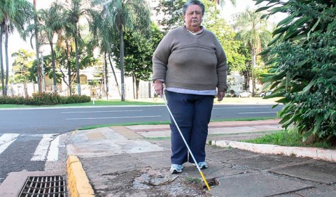 Mulher cega, andando com sua bengala, por uma calçada quebrada