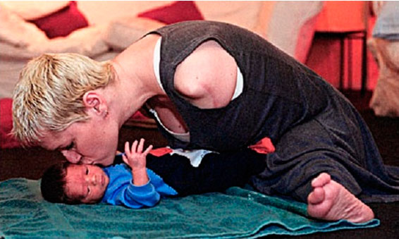 Mulher com deficiência, sem os braços, se curva para beijar seu bebê recém nascido