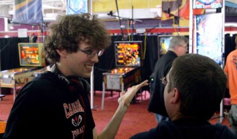 Rapaz autista conversa, animadamente, com outro jovem em um salão cheio de máquinas de fliperama