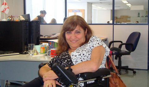 Mulher em cadeira de rodas sorri em um escritório