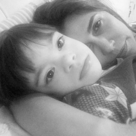 Foto em preto e branco de uma mãe abraçada a seu filho com Síndrome de Down, ambos na cama