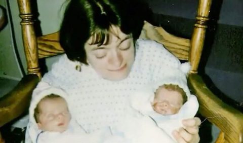 Foto antiga de uma mulher jovem sentada em uma cadeira amarela, segurando dois bebês recém nascidos em seus braços.