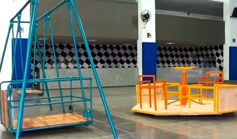 Foto de um ginásio escolar com dois brinquedos adaptados para crianças cadeirantes